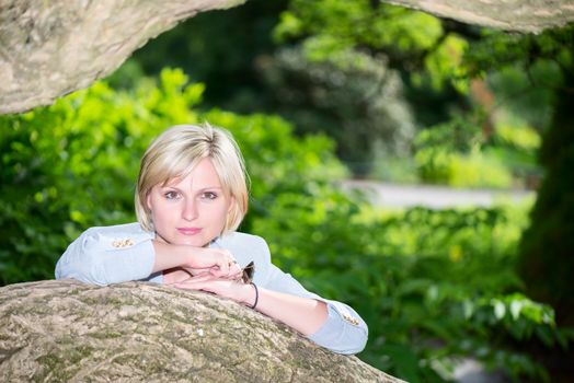 The portrait of the beautiful woman in green park near tree trunk