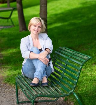 young woman sitting on bench in park smiling and looking into the camera