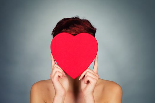 young woman hiding her face behind a red heart
