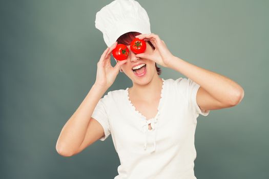young happy female cook holding tomatoes on her eyes