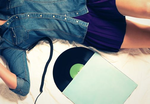 body of woman wearing jeans button down and a skirt on bed with a vinyl record