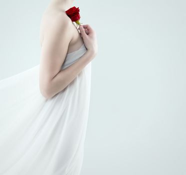 beautiful woman with a fabric drape holding red rose on her shoulder