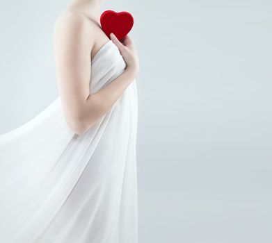 gorgeous woman in a white drape holding red heart to her shoulder
