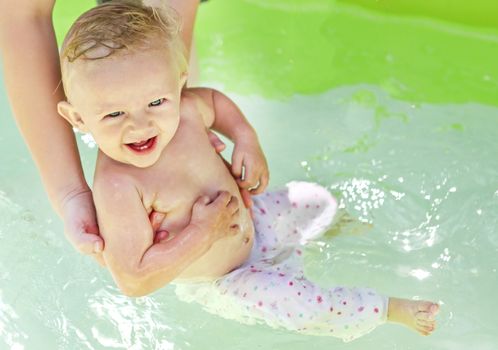 Parent bathing Cheerful Baby Boy in the Pool at Sunny Summer Day