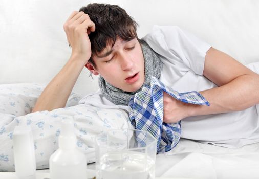 Young Man with Flu is Sneezing on the Bed with Handkerchief