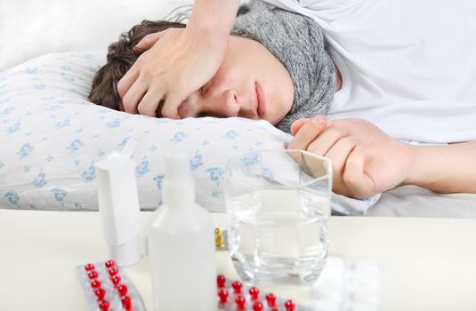 Sick Young Man sleeping on the Bed with Pills on foreground