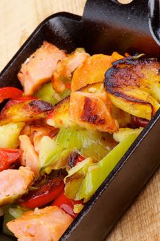 Homemade Salmon Stew with Potato, Red Bell Pepper, Leek and Carrot in Black Frying Pan closeup on Wooden background