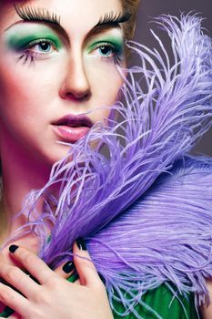 Attractive young girl with a fabulous makeup and feathers close-up portrait