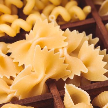 Various pasta  types in the wooden box on the table. Close up farfalle