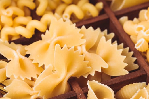 Various pasta  types in the wooden box on the table. Close up farfalle