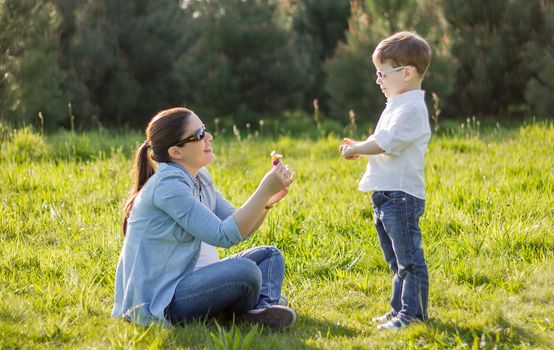 Happy cute son giving a bouquet of flowers to his mother in sunny field