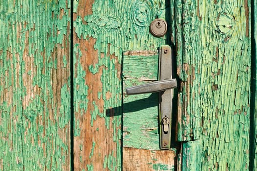 Old door handle on wooden door background with green ckracked paint 