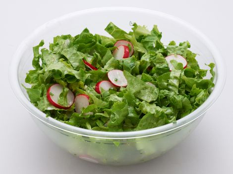 Green lettuce and red radish salad in transparent plastic cup on white