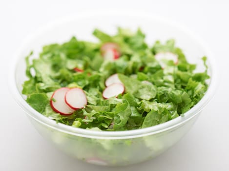 Green lettuce and red radish salad in transparent plastic cup on white