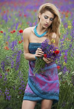 Beauty model girl in spring field with blossom flowers, fashion shooting on location