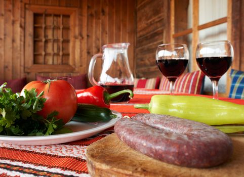 Wine, sasage and vegetables on table, traditional Bulgarian table setup with fresh food and glaases of res wine