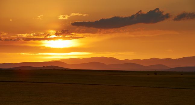 Landscape scenery with sunset over field and mountains