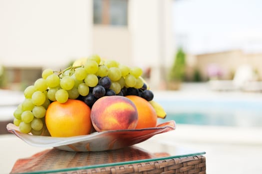 Ripe summer fruits on table near swimming pool