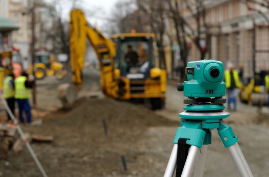 Theodolite, excavator and workers at road construcion site