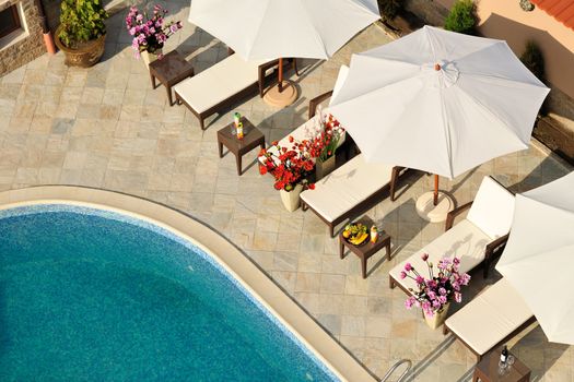 Swimming pool in small hotel yard with parasols and chaise-longues