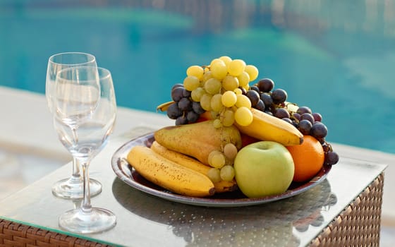 Fresh fruits and glasses near blue water