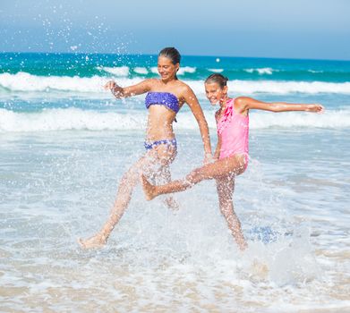 Cute girls friends running together in the beach shore on summer vacation