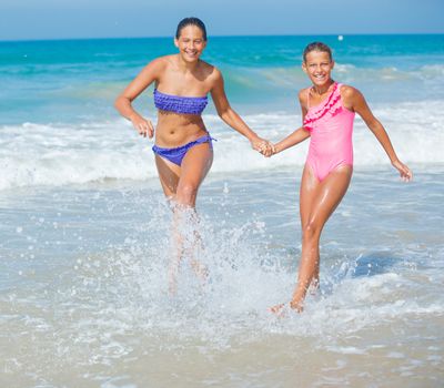 Cute girls friends running together in the beach shore on summer vacation