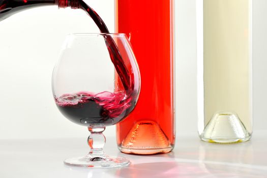 Filling a glass with red wine behind bottles