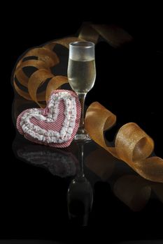 A glass of champagne, a golden streak and a heart made in patchwork on a black background