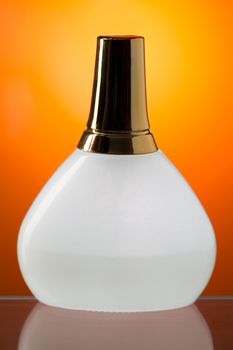 White bottle stands on the mirror surface. Orange background