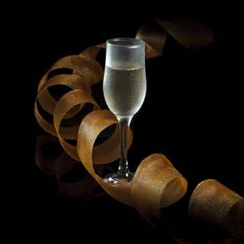 A glass of champagne and a golden streak on a black background