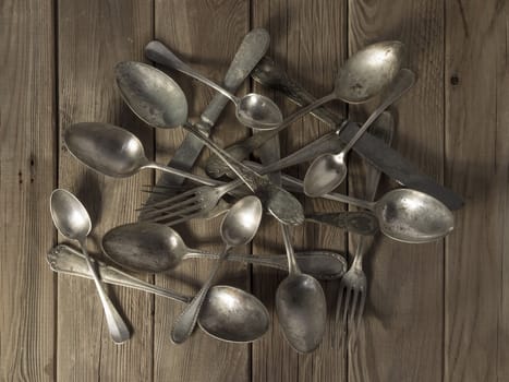A random group of old spoons, forks and knives on a worn wooden table