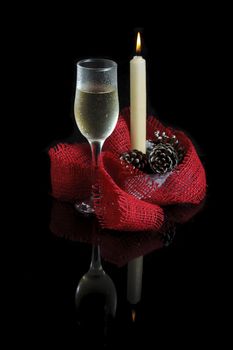 A glass of champagne, a candle and a red streak on a black background