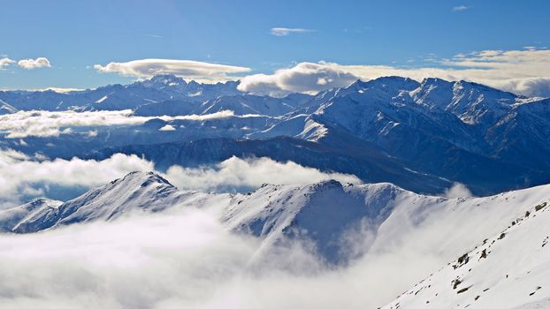 Aerial view of the alpine arc in a winter scenery with foggy valleys below. Italian Alps.