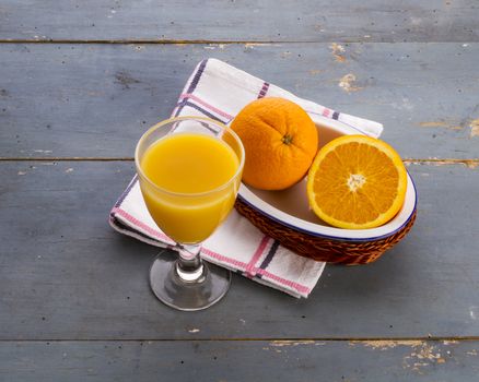 A glass with orange juice and a pair of oranges on an old blue table