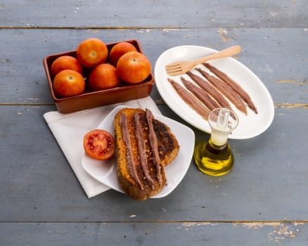 Still life with a catalan 'pa amb tomata' (bread or toast with tomato, salt and olive oil) with anchovies, on and old blue table