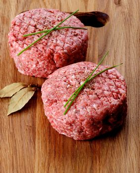 Ripe Raw Beef Burgers with Chives and Bay Leaf on Wooden Cutting Board closeup