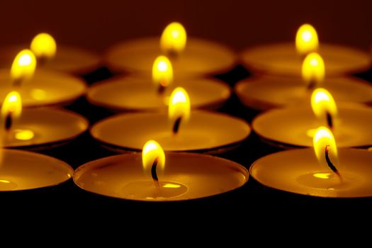 Tea lights candles with fire on dark background