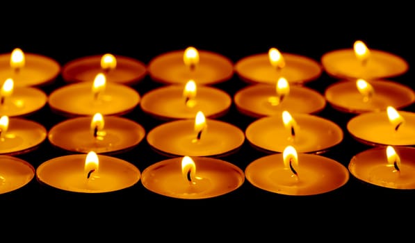 Tea lights candles with fire on dark background