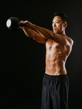 Photo of an Asian male exercising with a kettle bell over dark background. 