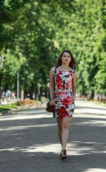 Young woman wearing a colourful dress walking in a park to the camera.