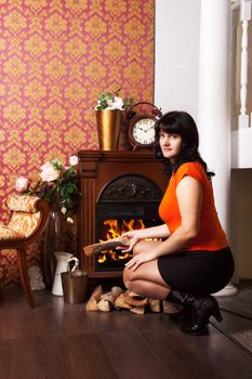 young beautiful woman in orange blouse sits near the fireplace