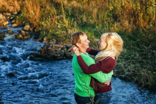 Young attractive couple embracing on the riverbank fall day