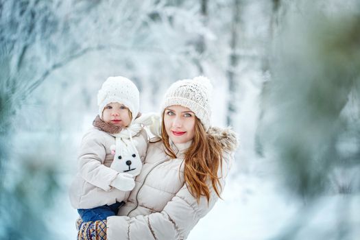 Young mother holding a daughter in a winter forest for a walk