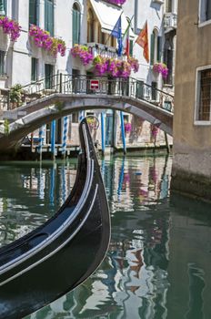 Gondola in a canal, with bridge and Venetian, Italian and European Union flags in the background. Venice, Italy.