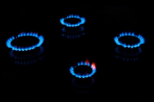 Blue gas flames from four stove burners in the dark