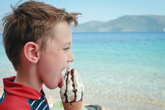 A five year old boy eating an ice cream at the beach