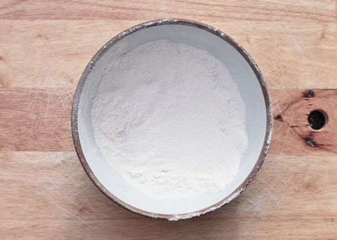 Bowl of plain white flour on a wooden surface