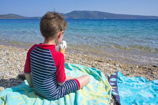 A five year old boy eating ice cream on the beach