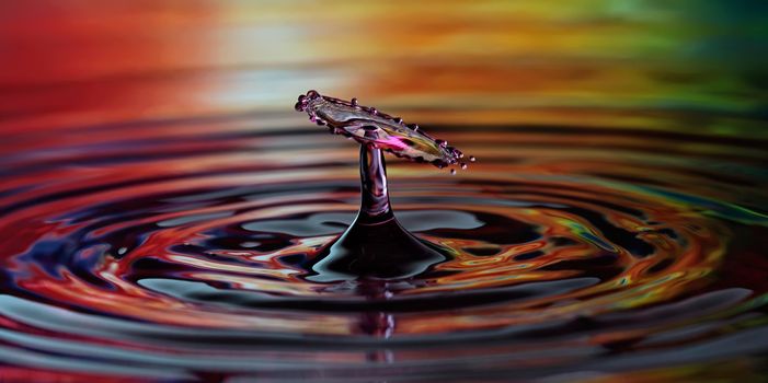 A clash of falling droplets create an umbrella on rainbow background